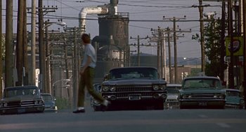 Movie still from “Tin Men” (1987), directed by Barry Levinson – A man walking across a street next to a car; Extreme Wide shot, Low angle