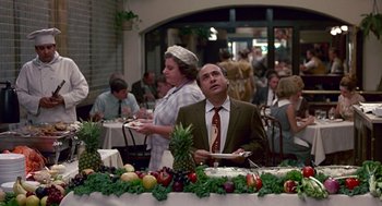 Movie still from “Tin Men” (1987), directed by Barry Levinson – A man and woman standing at a table with fruit on top of it; Wide shot, Over the shoulder angle