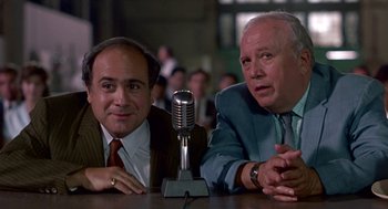 Movie still from “Tin Men” (1987), directed by Barry Levinson – A couple of men sitting at a table with a microphone; Medium shot, Low angle