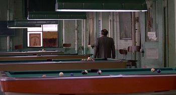 Movie still from “Tin Men” (1987), directed by Barry Levinson – A man standing in a room with a pool table; Wide shot, High angle