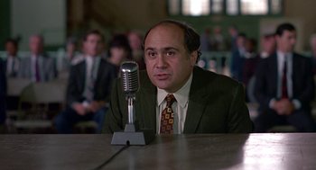 Movie still from “Tin Men” (1987), directed by Barry Levinson – A man sitting at a table in front of a microphone; Close Up shot, High angle