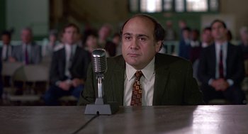 Movie still from “Tin Men” (1987), directed by Barry Levinson – A man sitting at a table in front of a microphone; Close Up shot, Low angle
