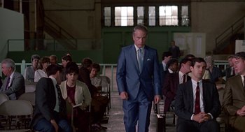 Movie still from “Tin Men” (1987), directed by Barry Levinson – A man in a blue suit walking in front of a group of people; Wide shot, Over the shoulder angle