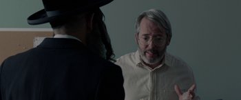 A man with a beard and glasses talking to another man