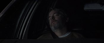 A man sleeping in the back seat of a car at night