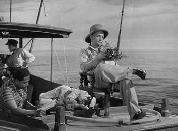 Movie still from “To Have and Have Not” (1944), directed by Howard Hawks – A man sitting on the back of a fishing boat; Wide shot, High angle
