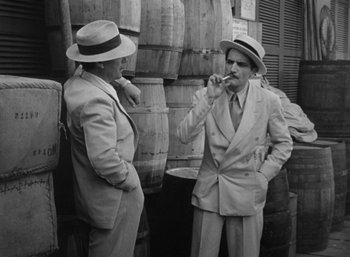 Movie still from “To Have and Have Not” (1944), directed by Howard Hawks – Two men standing next to each other wearing suits and hats; Medium shot, Over the shoulder angle