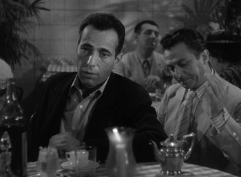 Movie still from “To Have and Have Not” (1944), directed by Howard Hawks – A man sitting at a table in front of another man; Medium shot, Over the shoulder angle