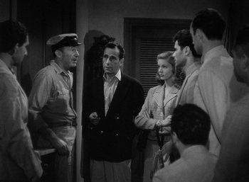 Movie still from “To Have and Have Not” (1944), directed by Howard Hawks – A black and white photo of a group of men standing next to each other; Medium shot, High angle