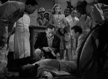 Movie still from “To Have and Have Not” (1944), directed by Howard Hawks – A group of people standing around a man laying on the ground; Medium shot, High angle