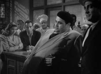 Movie still from “To Have and Have Not” (1944), directed by Howard Hawks – An old photo of a group of people in a room; Medium shot, High angle