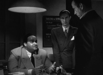 Movie still from “To Have and Have Not” (1944), directed by Howard Hawks – A group of men standing around a table; Medium shot, Over the shoulder angle
