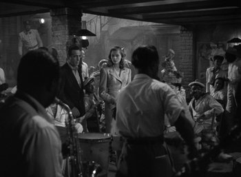 Movie still from “To Have and Have Not” (1944), directed by Howard Hawks – A black and white photo of a group of people in a room; Wide shot, Over the shoulder angle
