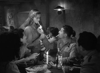 Movie still from “To Have and Have Not” (1944), directed by Howard Hawks – A group of people sitting around a table with candles; Medium shot, Over the shoulder angle