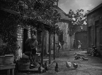 Movie still from “To Have and Have Not” (1944), directed by Howard Hawks – An old photo of a man sitting on a bench with chickens in the background; Wide shot, High angle
