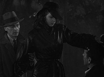 Movie still from “To Have and Have Not” (1944), directed by Howard Hawks – A man and a woman dressed in black and wearing a hat; Medium shot, Over the shoulder angle
