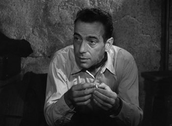 Movie still from “To Have and Have Not” (1944), directed by Howard Hawks – A black - and - white photo of a man smoking a cigarette; Close Up shot, High angle