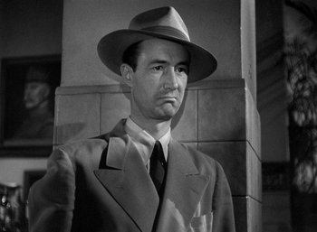 Movie still from “To Have and Have Not” (1944), directed by Howard Hawks – A man wearing a suit and a hat standing next to a wall; Close Up shot, Low angle