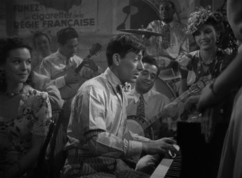 Movie still from “To Have and Have Not” (1944), directed by Howard Hawks – A man playing a piano in front of a group of people; Medium shot, High angle