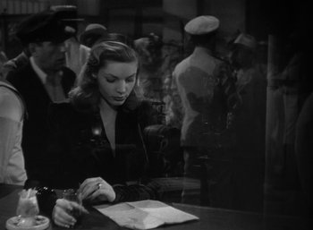 Movie still from “To Have and Have Not” (1944), directed by Howard Hawks – A woman sitting at a table writing on a piece of paper; Medium shot, High angle