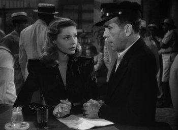 Movie still from “To Have and Have Not” (1944), directed by Howard Hawks – A man and a woman sitting at a table in front of each other; Medium shot, Low angle