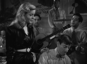 Movie still from “To Have and Have Not” (1944), directed by Howard Hawks – A woman standing next to a man holding a guitar; Medium shot, Over the shoulder angle