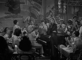 Movie still from “To Have and Have Not” (1944), directed by Howard Hawks – A group of people sitting in a room with musical instruments; Wide shot, High angle