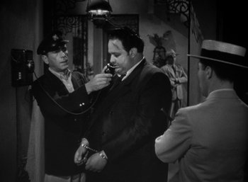 Movie still from “To Have and Have Not” (1944), directed by Howard Hawks – A man in a suit is being handcuffed by another man; Medium shot, Low angle