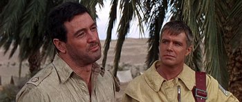 Movie still from “Tobruk” (1967), directed by Arthur Hiller – Two men standing next to each other near a palm tree; Close Up shot, Low angle