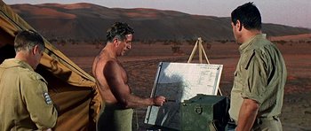 Movie still from “Tobruk” (1967), directed by Arthur Hiller – A man standing in front of an easel holding a map; Medium shot, Over the shoulder angle