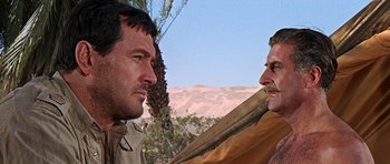 Movie still from “Tobruk” (1967), directed by Arthur Hiller – Two men are standing next to each other in the desert; Close Up shot, Low angle