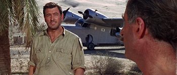 Movie still from “Tobruk” (1967), directed by Arthur Hiller – A man standing in front of an airplane on a dirt field; Medium shot, Over the shoulder angle