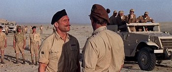 Movie still from “Tobruk” (1967), directed by Arthur Hiller – Two men are standing in the desert talking to each other; Medium shot, Over the shoulder angle