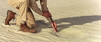 Movie still from “Tobruk” (1967), directed by Arthur Hiller – A man is digging a hole in the sand; Extreme Close Up shot, Overhead angle