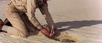 Movie still from “Tobruk” (1967), directed by Arthur Hiller – A man kneeling down in the sand with his hands on the ground; Medium shot, Overhead angle