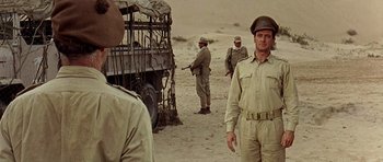 Movie still from “Tobruk” (1967), directed by Arthur Hiller – A group of men standing next to each other in the desert; Medium shot, Over the shoulder angle