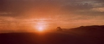 Movie still from “Tobruk” (1967), directed by Arthur Hiller – The sun is setting over a field with a house in the distance; Extreme Wide shot, Low angle