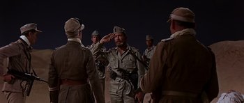 Movie still from “Tobruk” (1967), directed by Arthur Hiller – A group of men in uniform saluting in the dark; Medium shot, Low angle