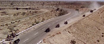 Movie still from “Tobruk” (1967), directed by Arthur Hiller – A group of people riding motorcycles down a road; Extreme Wide shot, High angle