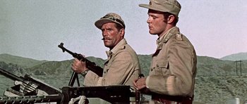 Movie still from “Tobruk” (1967), directed by Arthur Hiller – Two men in military uniforms are standing next to each other in a field; Medium shot, Low angle