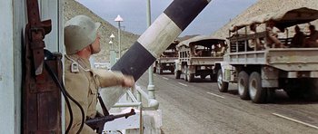 Movie still from “Tobruk” (1967), directed by Arthur Hiller – A man holding a gun while standing next to a truck; Medium shot, Over the shoulder angle
