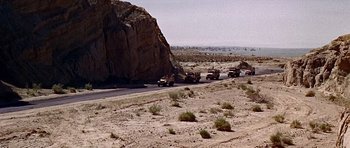 Movie still from “Tobruk” (1967), directed by Arthur Hiller – A group of trucks driving down a road next to rocks; Extreme Wide shot, High angle
