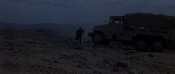 Movie still from “Tobruk” (1967), directed by Arthur Hiller – A man walking across a barren field next to a truck; Extreme Wide shot, Low angle
