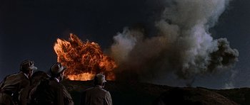 Movie still from “Tobruk” (1967), directed by Arthur Hiller – A man standing in front of a large fire at night; Extreme Wide shot, Low angle