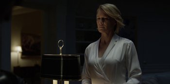 Movie still from “House of Cards” (2013), created by Beau Willimon – A woman standing in front of a lamp in a dimly - lit room; Medium shot, Low angle