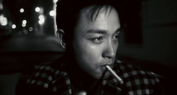 Movie still from “Happy Together” (1997), directed by Kar-Wai Wong – A black and white photo of a man smoking a cigarette; Close Up shot, Low angle