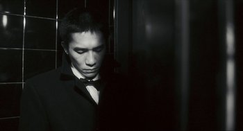 Movie still from “Happy Together” (1997), directed by Kar-Wai Wong – A man in a suit and bow tie standing in front of a wall; Close Up shot, Low angle