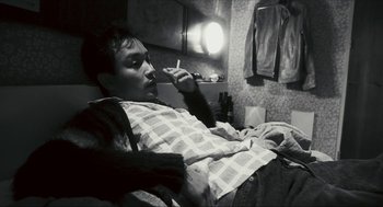 Movie still from “Happy Together” (1997), directed by Kar-Wai Wong – A man sitting on a bed smoking a cigarette; Medium shot, High angle