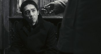 Movie still from “Happy Together” (1997), directed by Kar-Wai Wong – A man in a black coat is sitting in front of another man holding a cell phone; Close Up shot, Over the shoulder angle