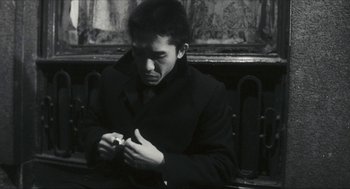 Movie still from “Happy Together” (1997), directed by Kar-Wai Wong – A man sitting on a bench looking down at a piece of paper; Close Up shot, Low angle